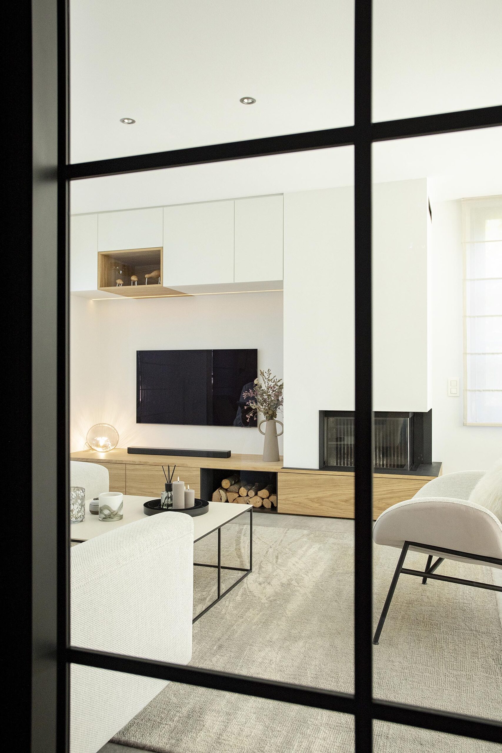 Séjour contemporain avec meuble sur mesure intégrant le foyer et la télévision, chêne clair et accents noirs, dans une ambiance chaleureuse et raffinée
