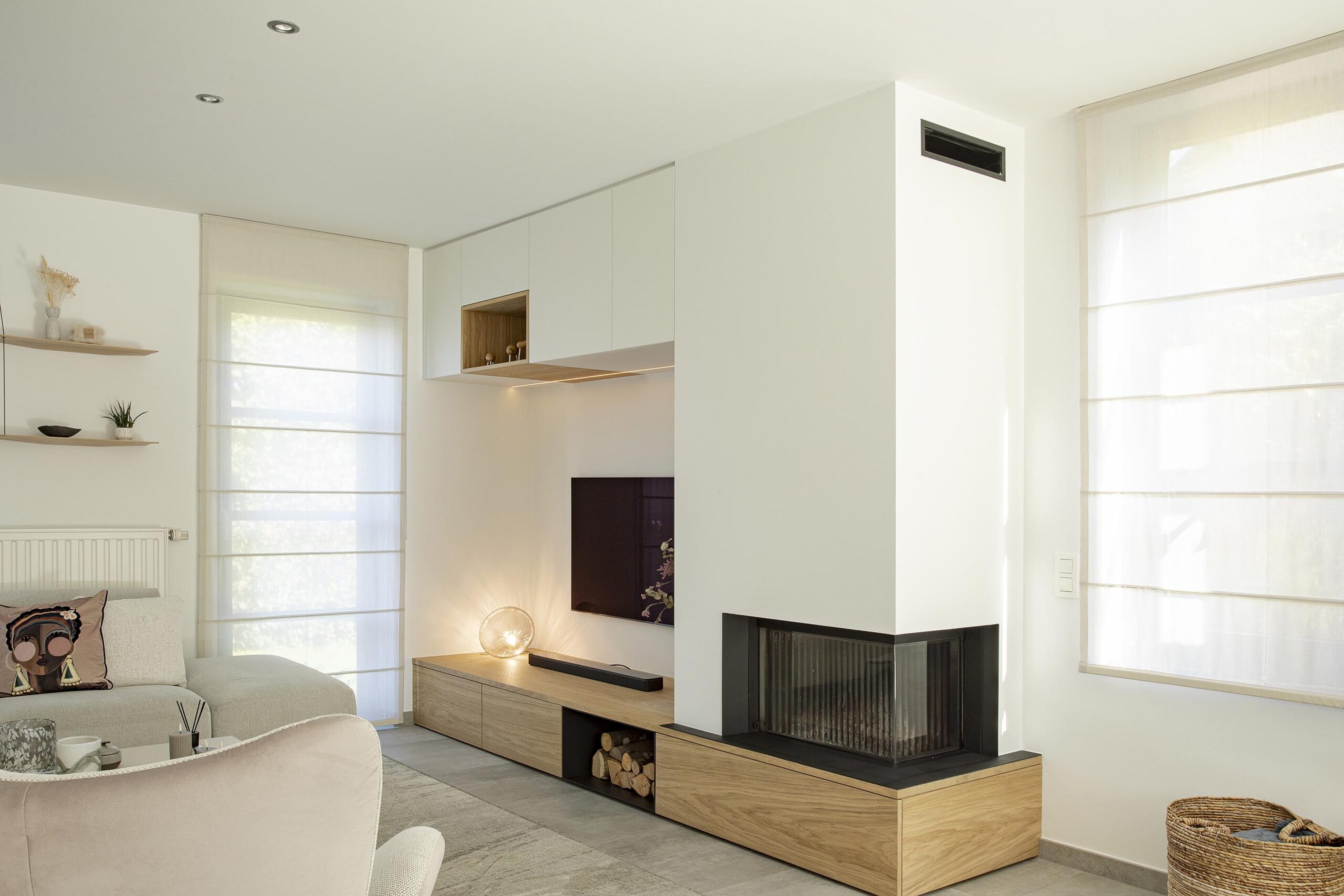 Séjour contemporain avec meuble sur mesure intégrant le foyer et la télévision, chêne clair et accents noirs, dans une ambiance chaleureuse et raffinée