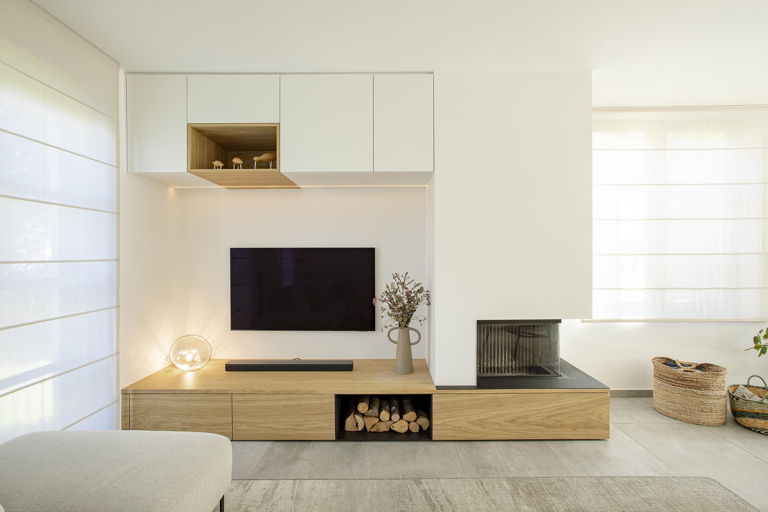 Séjour contemporain avec meuble sur mesure intégrant le foyer et la télévision, chêne clair et accents noirs, dans une ambiance chaleureuse et raffinée