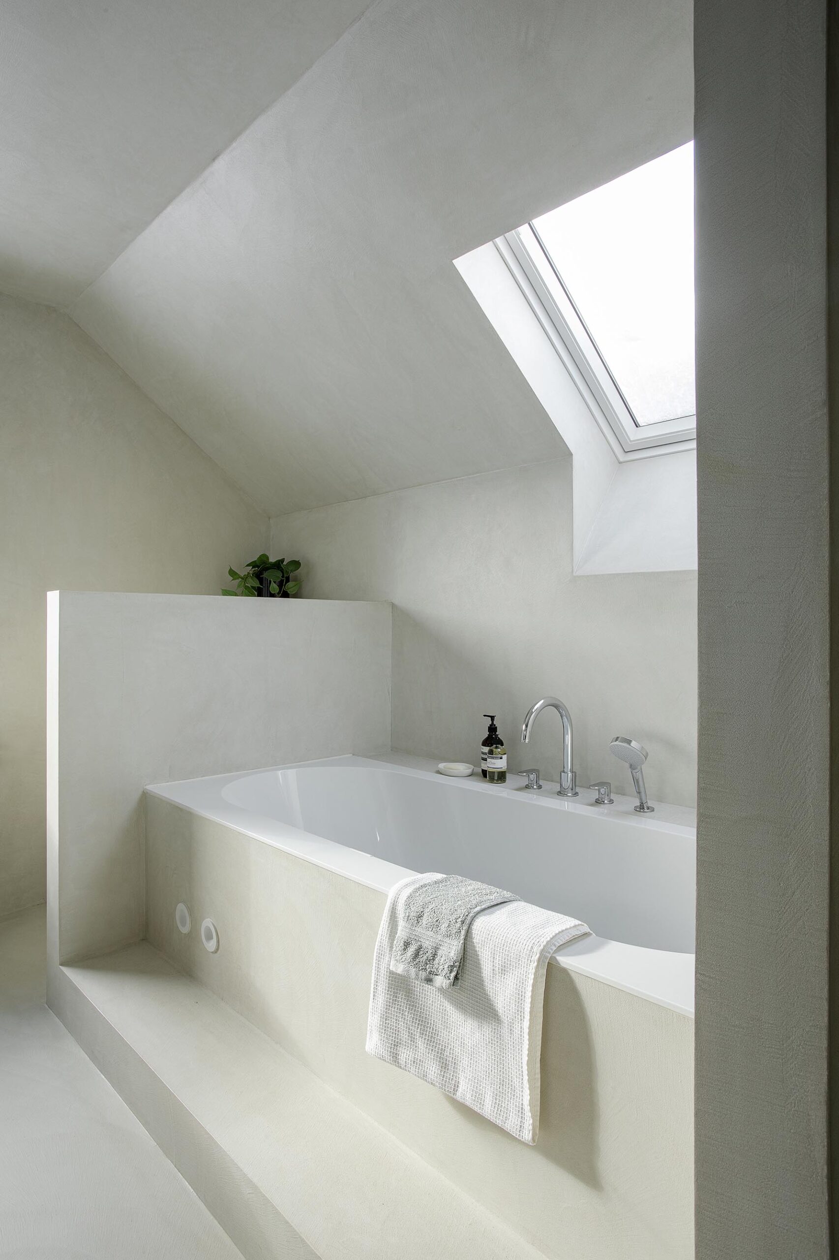 Salle de bains des enfants avec baignoire centrale, structure sur mesure en U et marche intégrée, dans une composition contemporaine, intime et élégante
