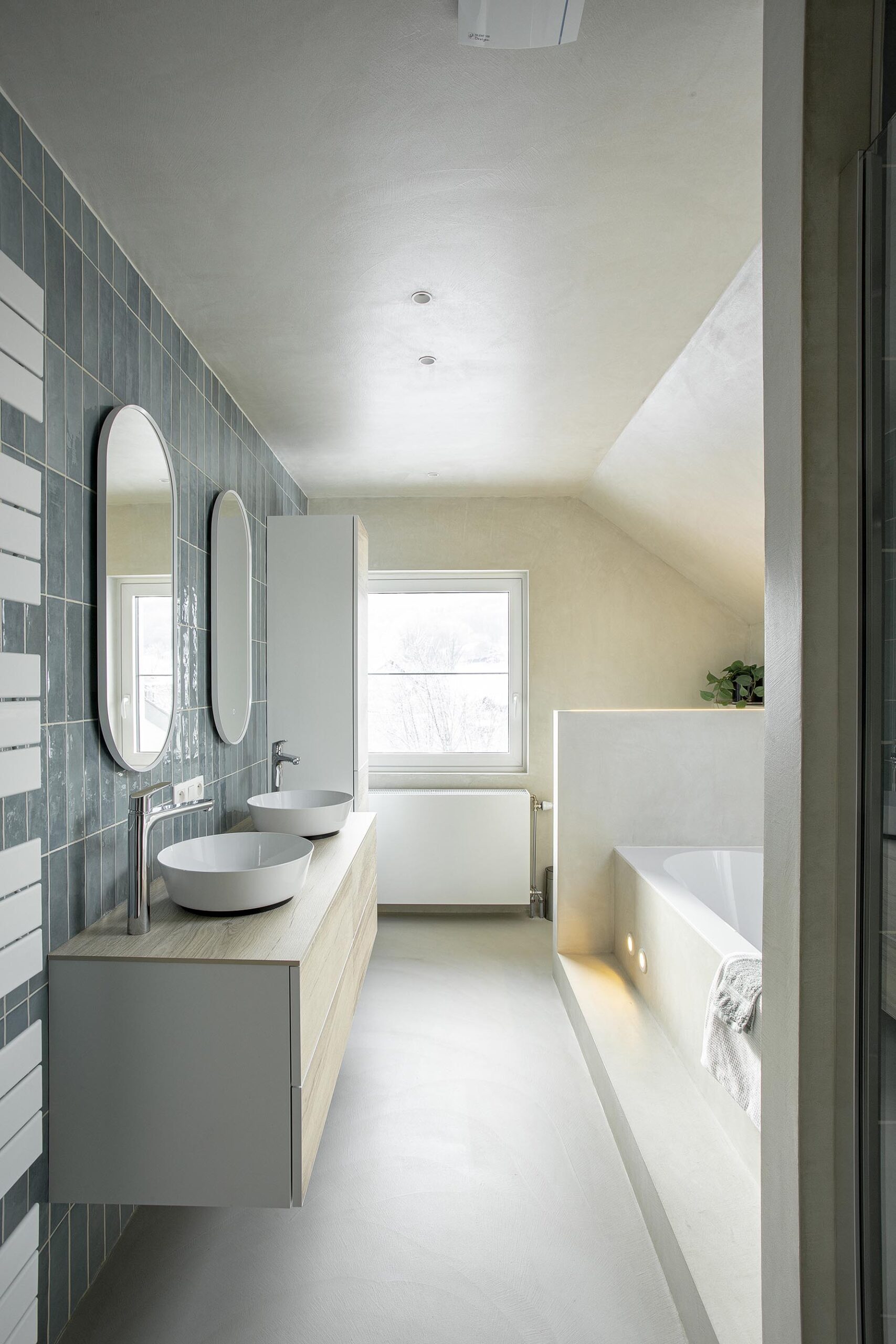 Salle de bains des enfants avec baignoire centrale, structure sur mesure en U et marche intégrée, dans une composition contemporaine, intime et élégante