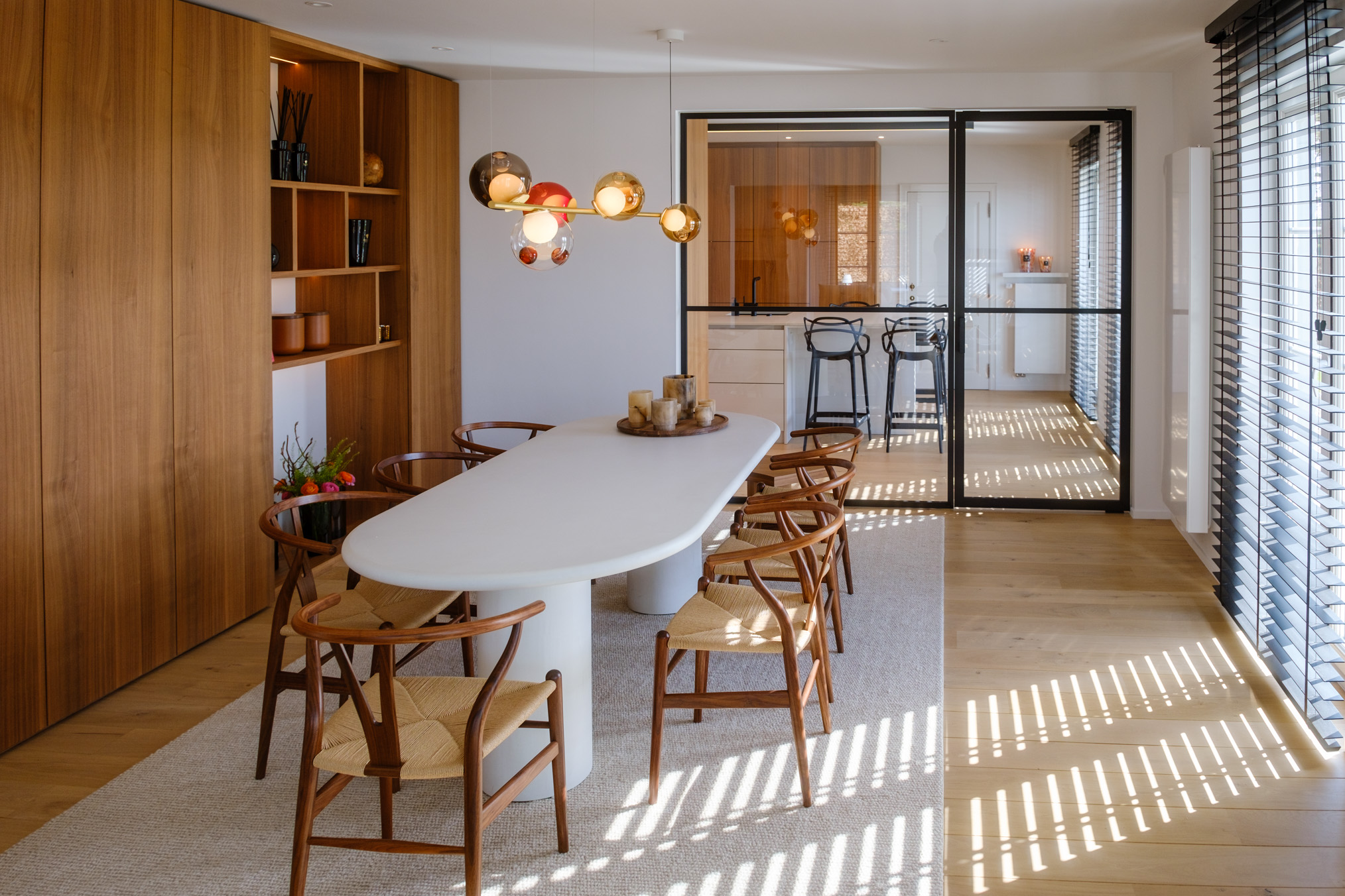 Salle à manger contemporaine avec mobilier sur mesure en noyer, table sculpturale et verrière ouvrant sur la cuisine.