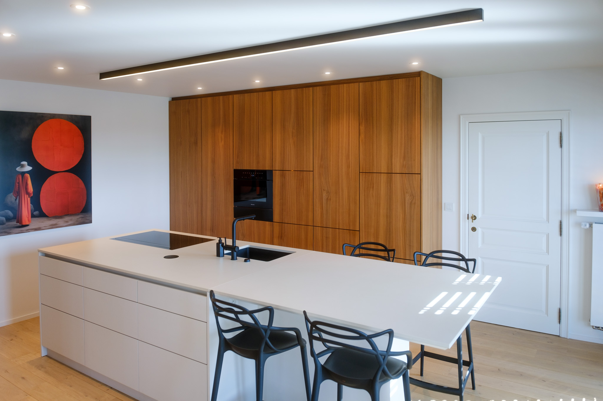 Salle à manger contemporaine avec mobilier sur mesure en noyer, table sculpturale et verrière ouvrant sur la cuisine.