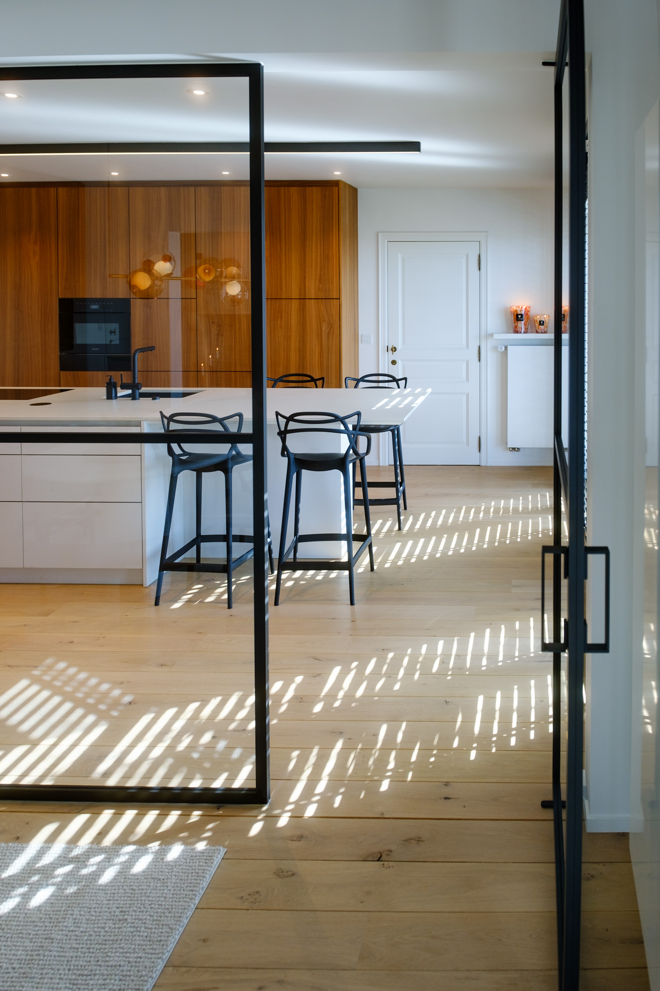 Salle à manger contemporaine avec mobilier sur mesure en noyer, table sculpturale et verrière ouvrant sur la cuisine.