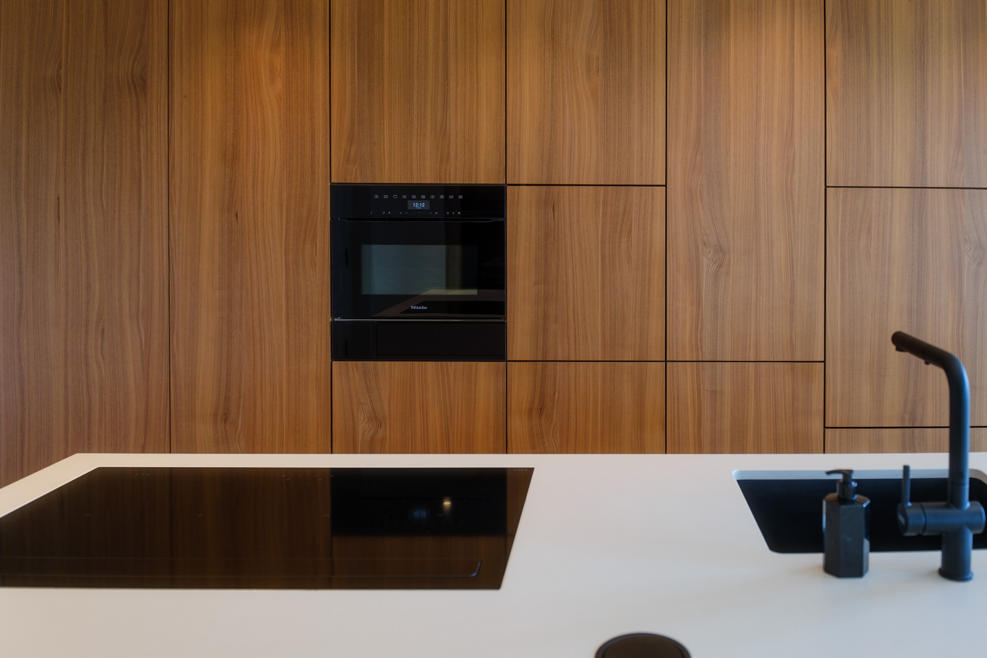 Salle à manger contemporaine avec mobilier sur mesure en noyer, table sculpturale et verrière ouvrant sur la cuisine.