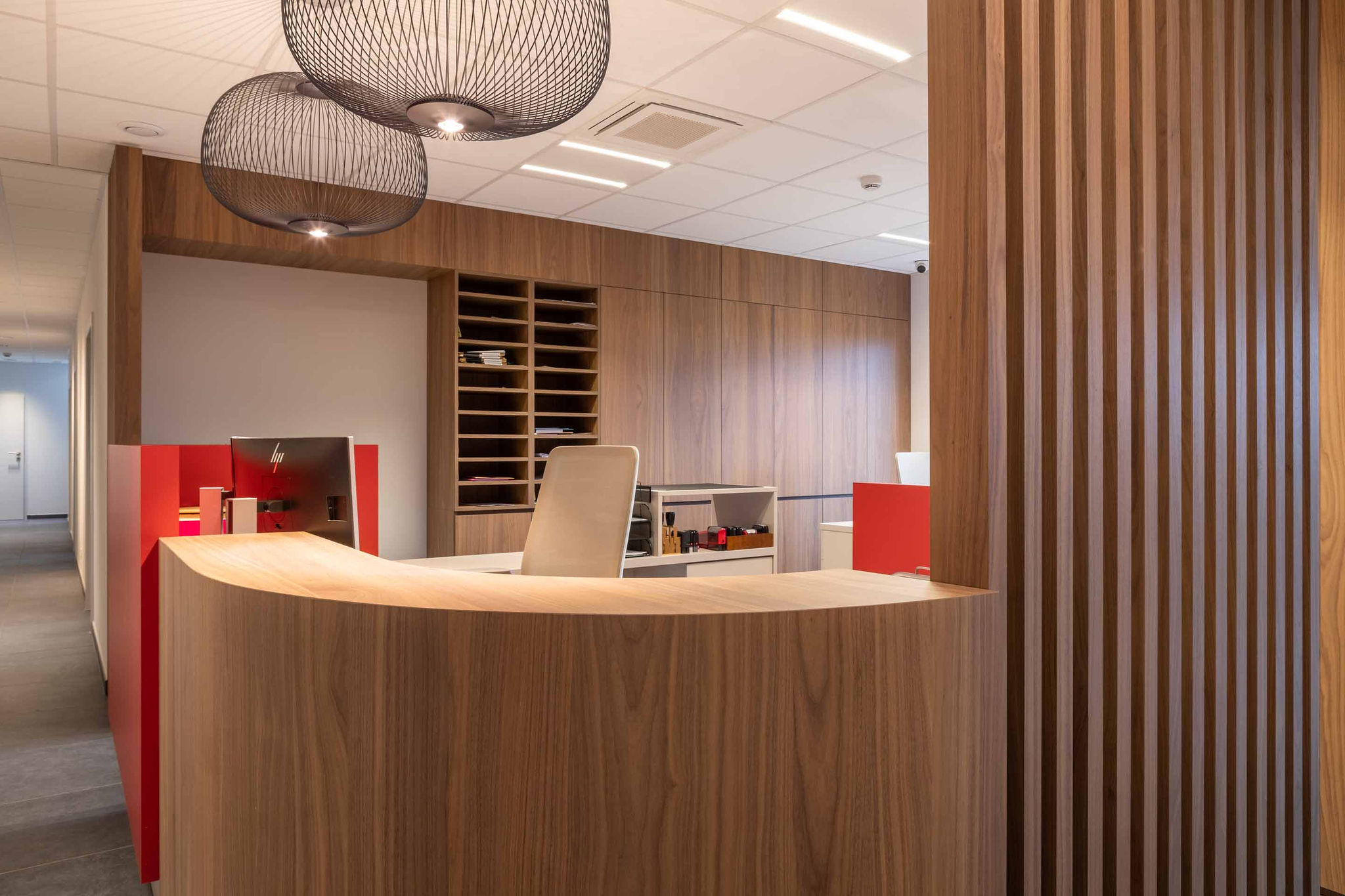 Aménagement intérieur contemporain d’une étude notariale à Namur, avec mobilier en noyer, lignes courbes et accents rouge carmin dans une ambiance professionnelle haut de gamme