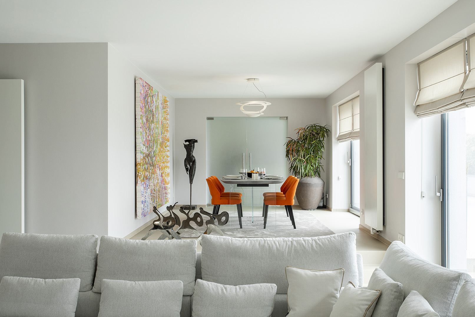 Salle à manger contemporaine ouverte sur le séjour, avec fauteuils orange, œuvres d’art et mobilier design, projet d’architecture d’intérieur à Arlon