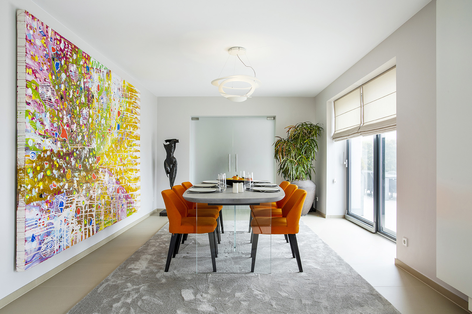 Salle à manger contemporaine ouverte sur le séjour, avec fauteuils orange, œuvres d’art et mobilier design, projet d’architecture d’intérieur à Arlon