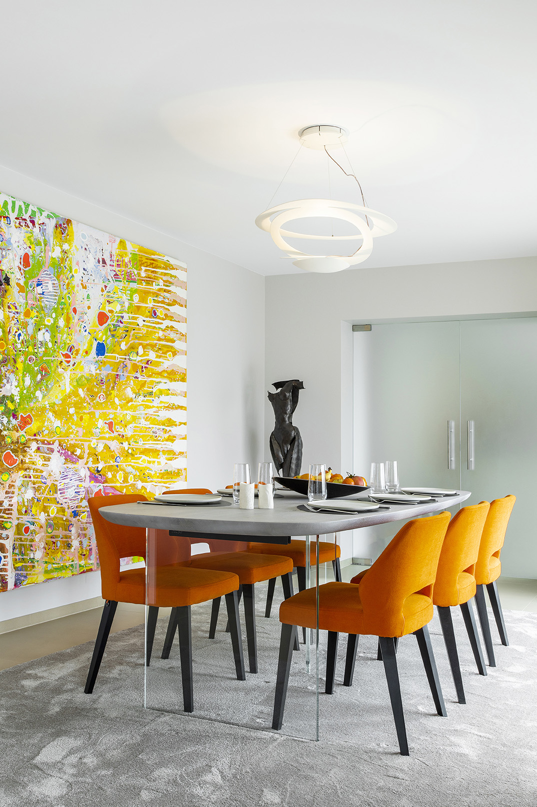 Salle à manger contemporaine ouverte sur le séjour, avec fauteuils orange, œuvres d’art et mobilier design, projet d’architecture d’intérieur à Arlon