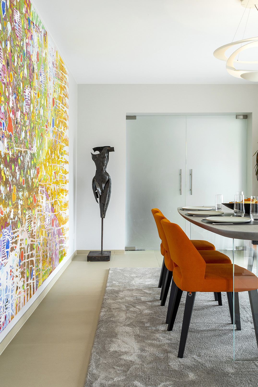 Salle à manger contemporaine ouverte sur le séjour, avec fauteuils orange, œuvres d’art et mobilier design, projet d’architecture d’intérieur à Arlon