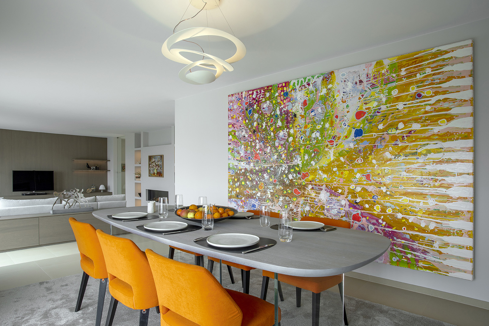 Salle à manger contemporaine ouverte sur le séjour, avec fauteuils orange, œuvres d’art et mobilier design, projet d’architecture d’intérieur à Arlon