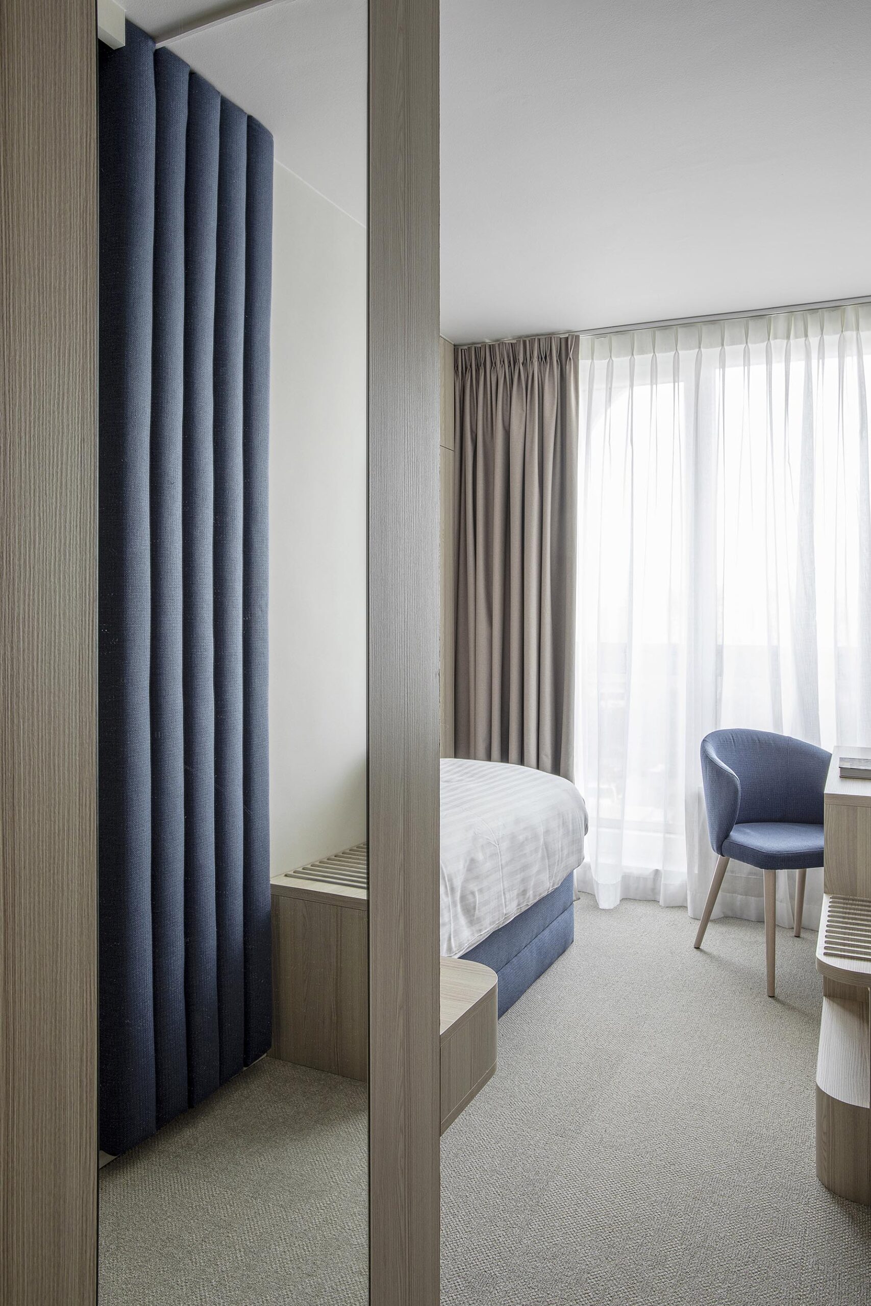 Chambre d’hôtel contemporaine aux 3 Clés à Gembloux, avec tête de lit bleue sur mesure, habillage mural en bois clair et éclairage indirect chaleureux