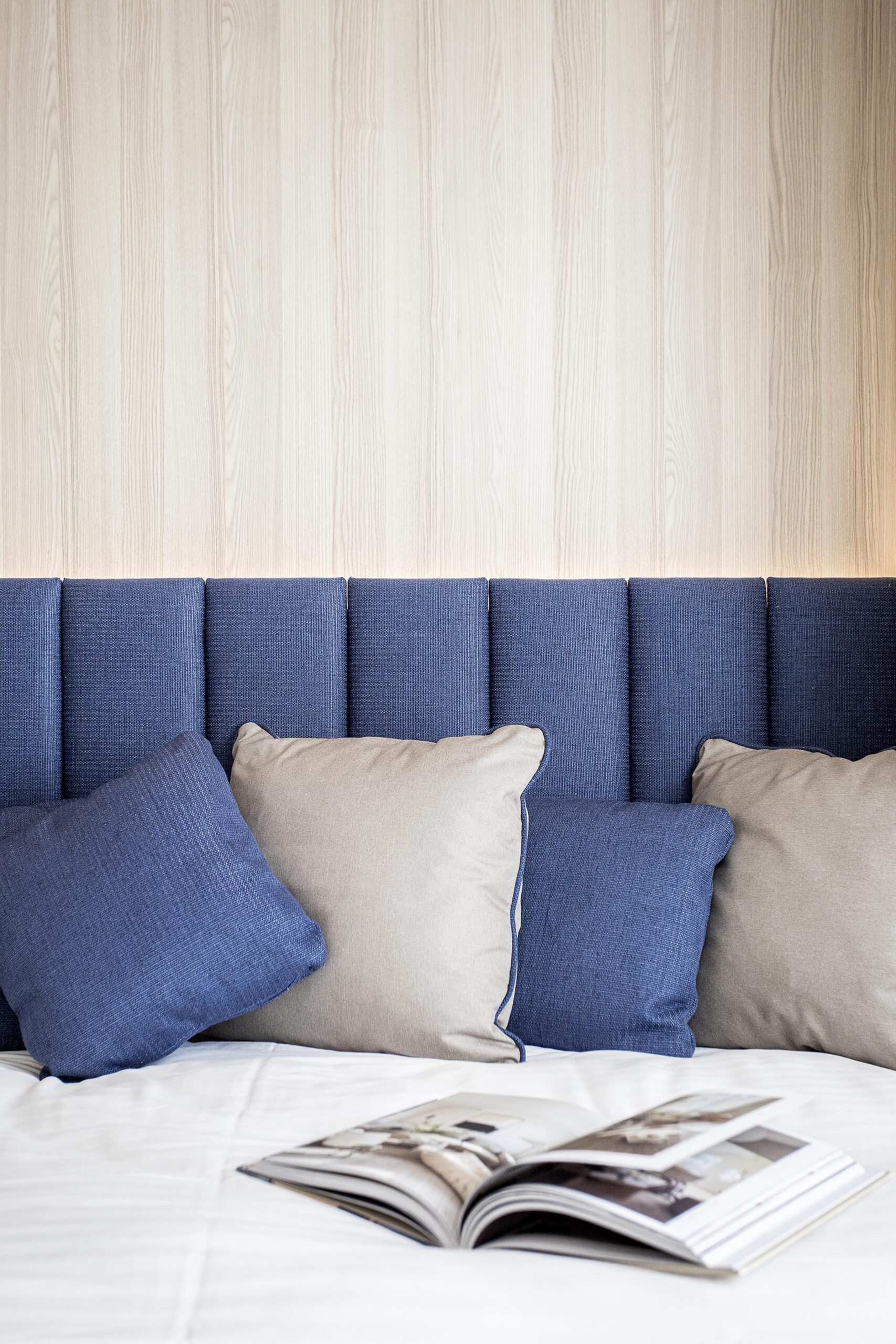 Chambre d’hôtel contemporaine aux 3 Clés à Gembloux, avec tête de lit bleue sur mesure, habillage mural en bois clair et éclairage indirect chaleureux.