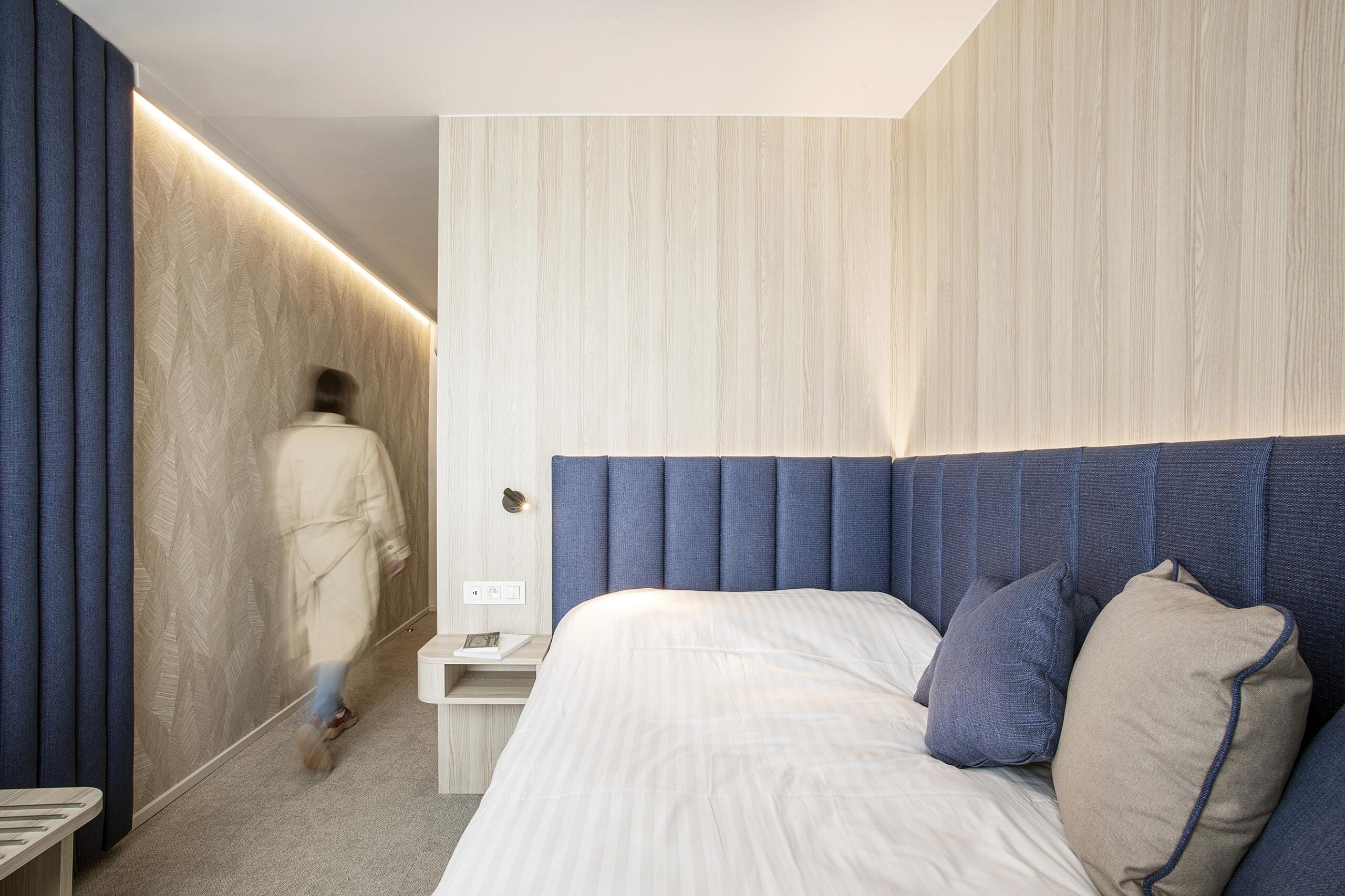Chambre d’hôtel contemporaine aux 3 Clés à Gembloux, avec tête de lit bleue sur mesure, habillage mural en bois clair et éclairage indirect chaleureux