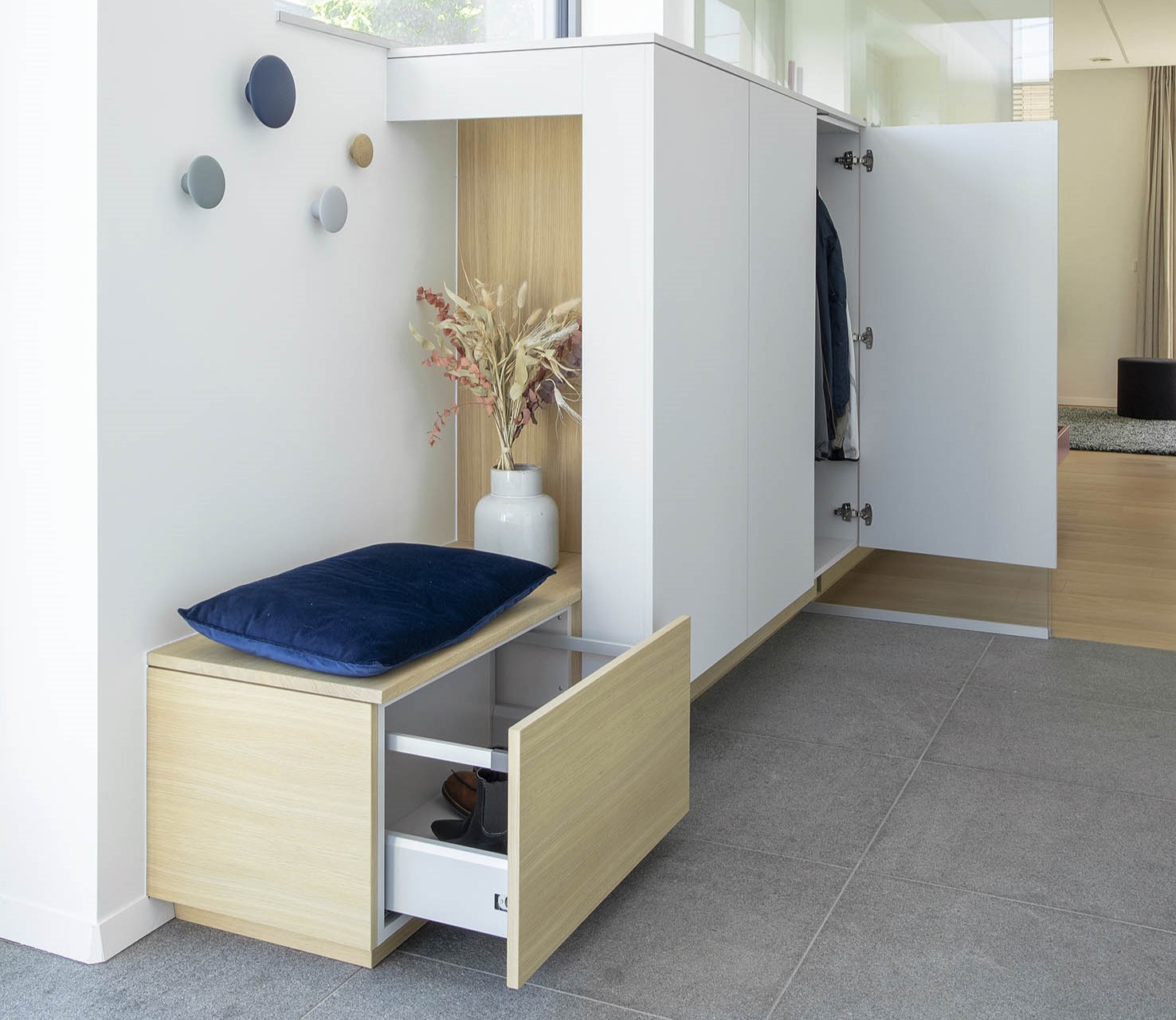 Hall d’entrée contemporain avec mobilier sur mesure en bois clair, banquette intégrée et paroi vitrée, projet d’architecture d’intérieur à Arlon.