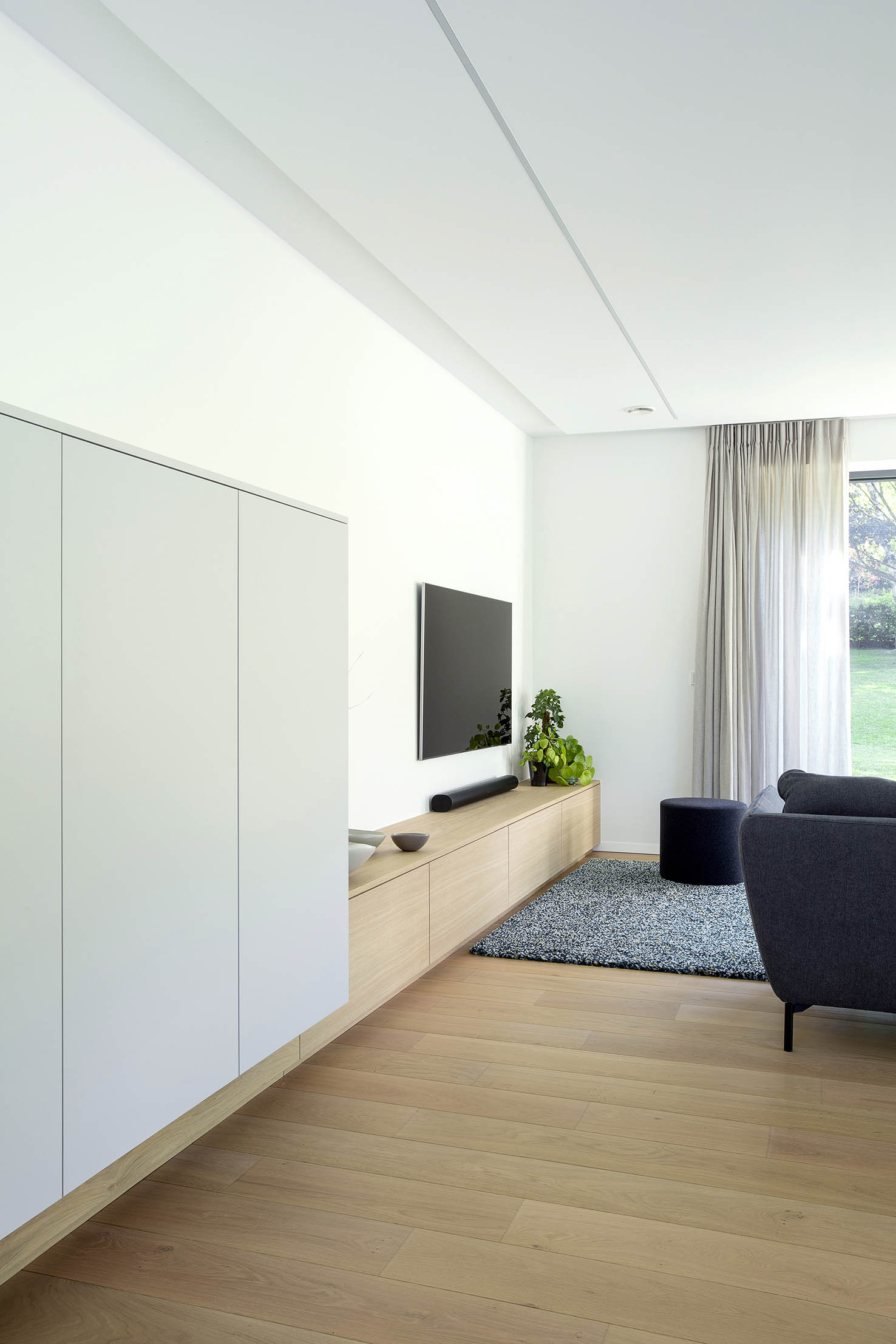 Hall d’entrée contemporain avec mobilier sur mesure en bois clair, banquette intégrée et paroi vitrée, projet d’architecture d’intérieur à Arlon.