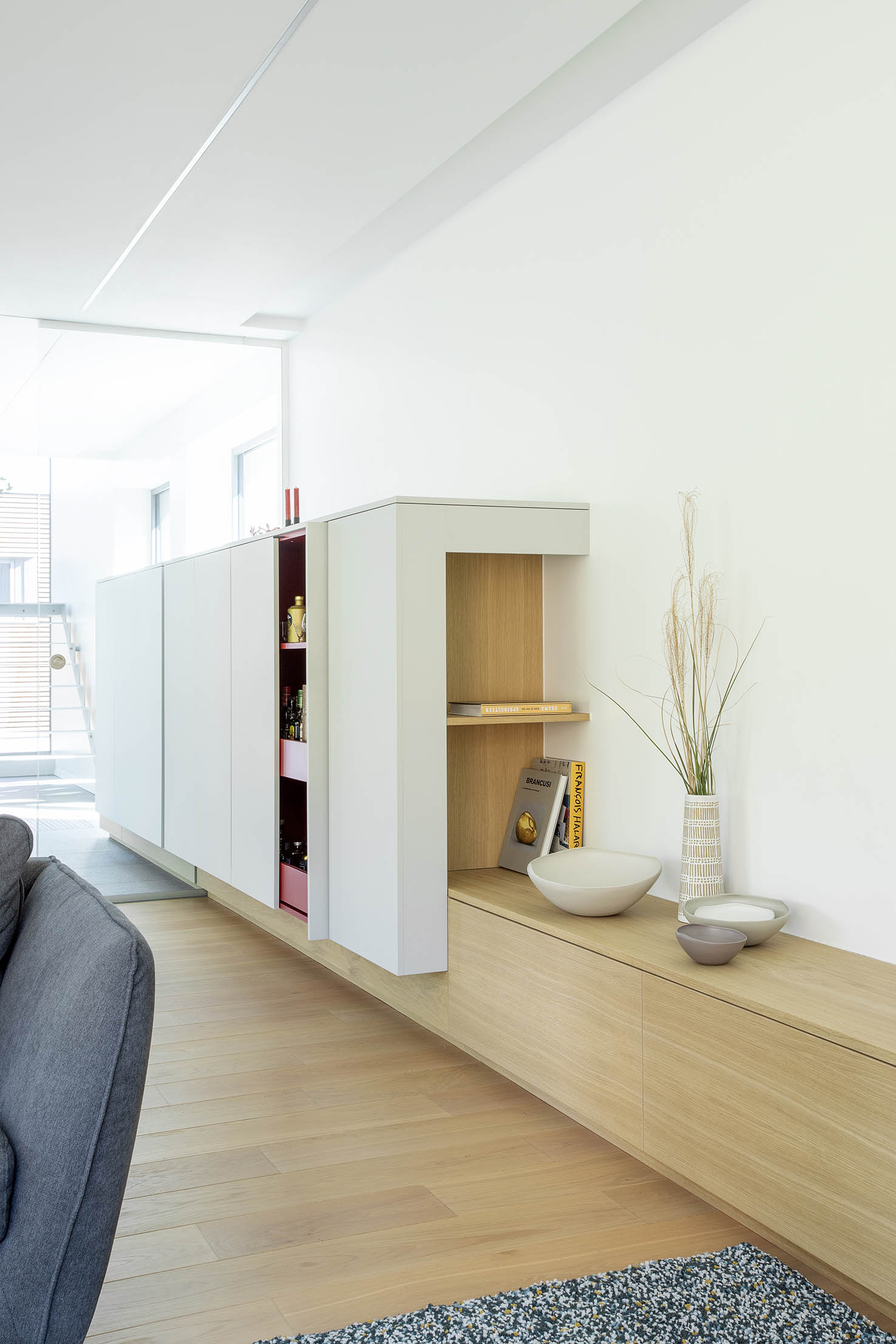 Hall d’entrée contemporain avec mobilier sur mesure en bois clair, banquette intégrée et paroi vitrée, projet d’architecture d’intérieur à Arlon.