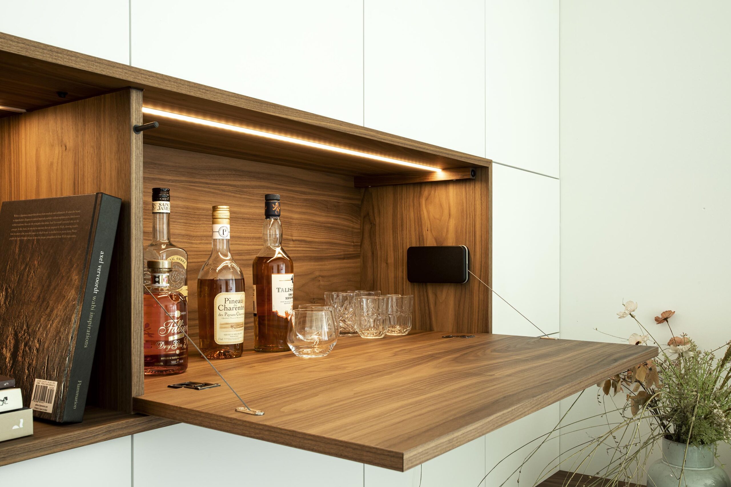 Salon contemporain lumineux avec mobilier sur mesure blanc et bois, niche intégrée éclairée et grandes baies vitrées, projet d’architecture d’intérieur à Arlon