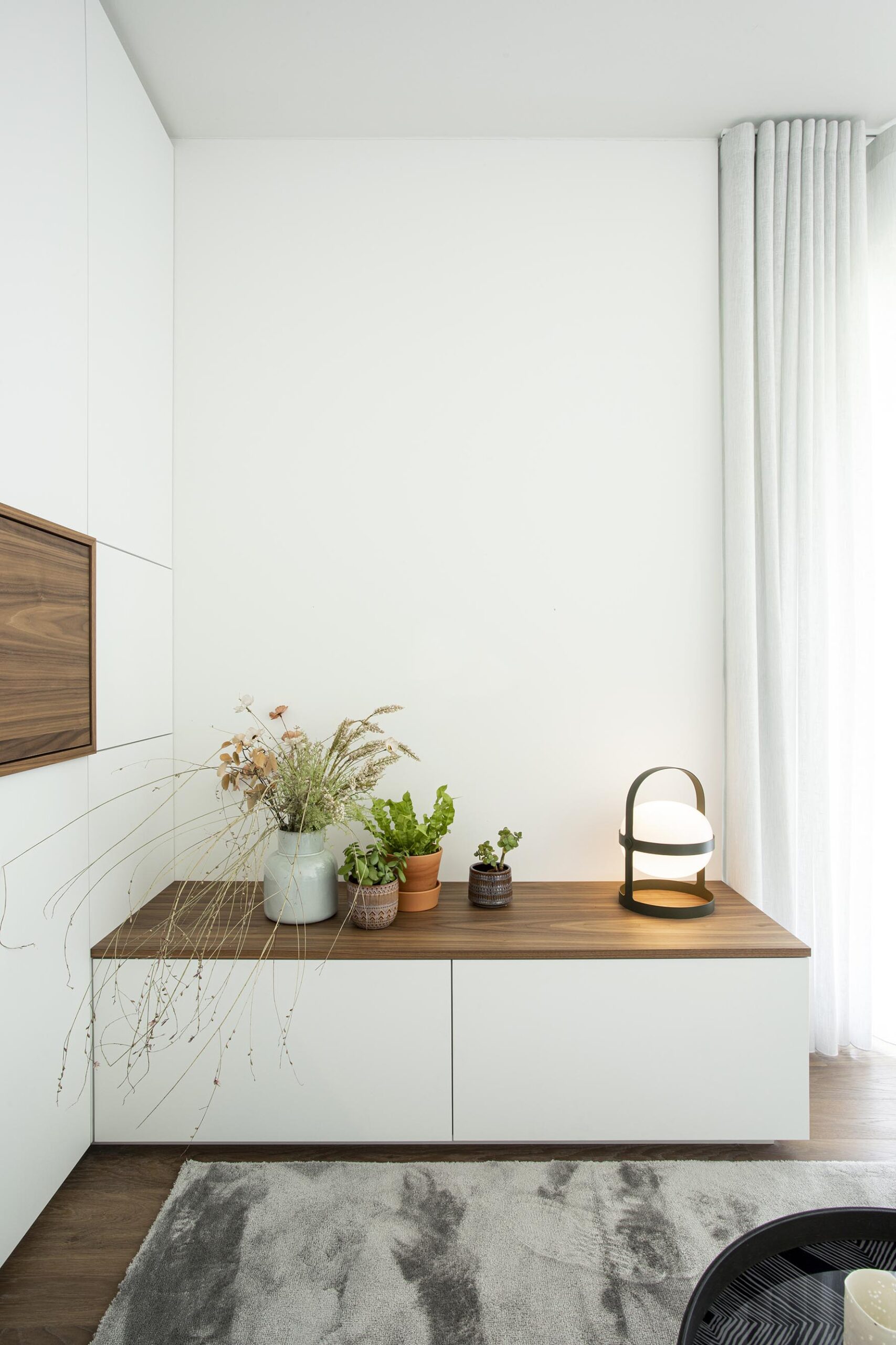 Salon contemporain lumineux avec mobilier sur mesure blanc et bois, niche intégrée éclairée et grandes baies vitrées, projet d’architecture d’intérieur à Arlon