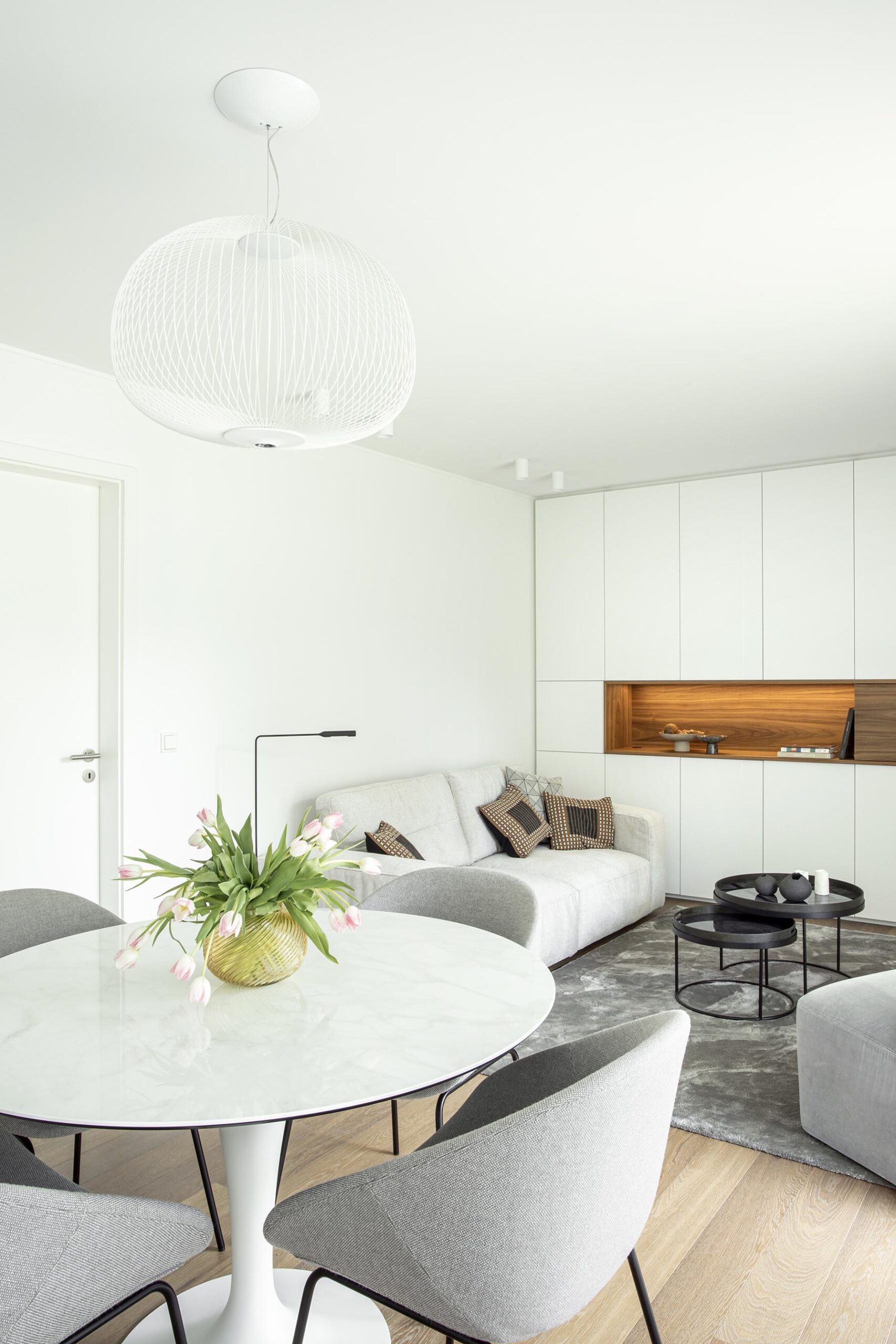 Salon contemporain lumineux avec mobilier sur mesure blanc et bois, niche intégrée éclairée et grandes baies vitrées, projet d’architecture d’intérieur à Arlon