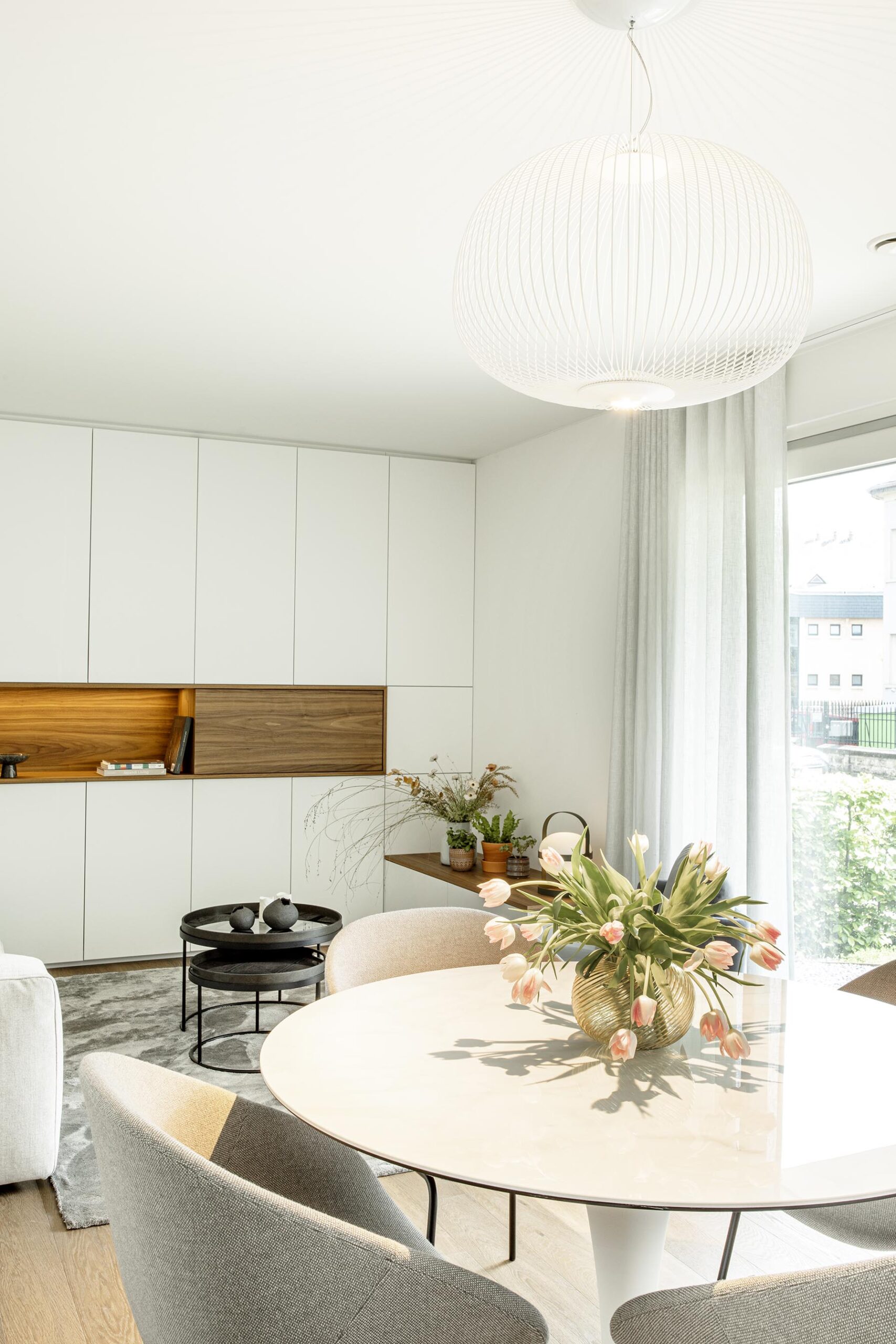Salon contemporain lumineux avec mobilier sur mesure blanc et bois, niche intégrée éclairée et grandes baies vitrées, projet d’architecture d’intérieur à Arlon