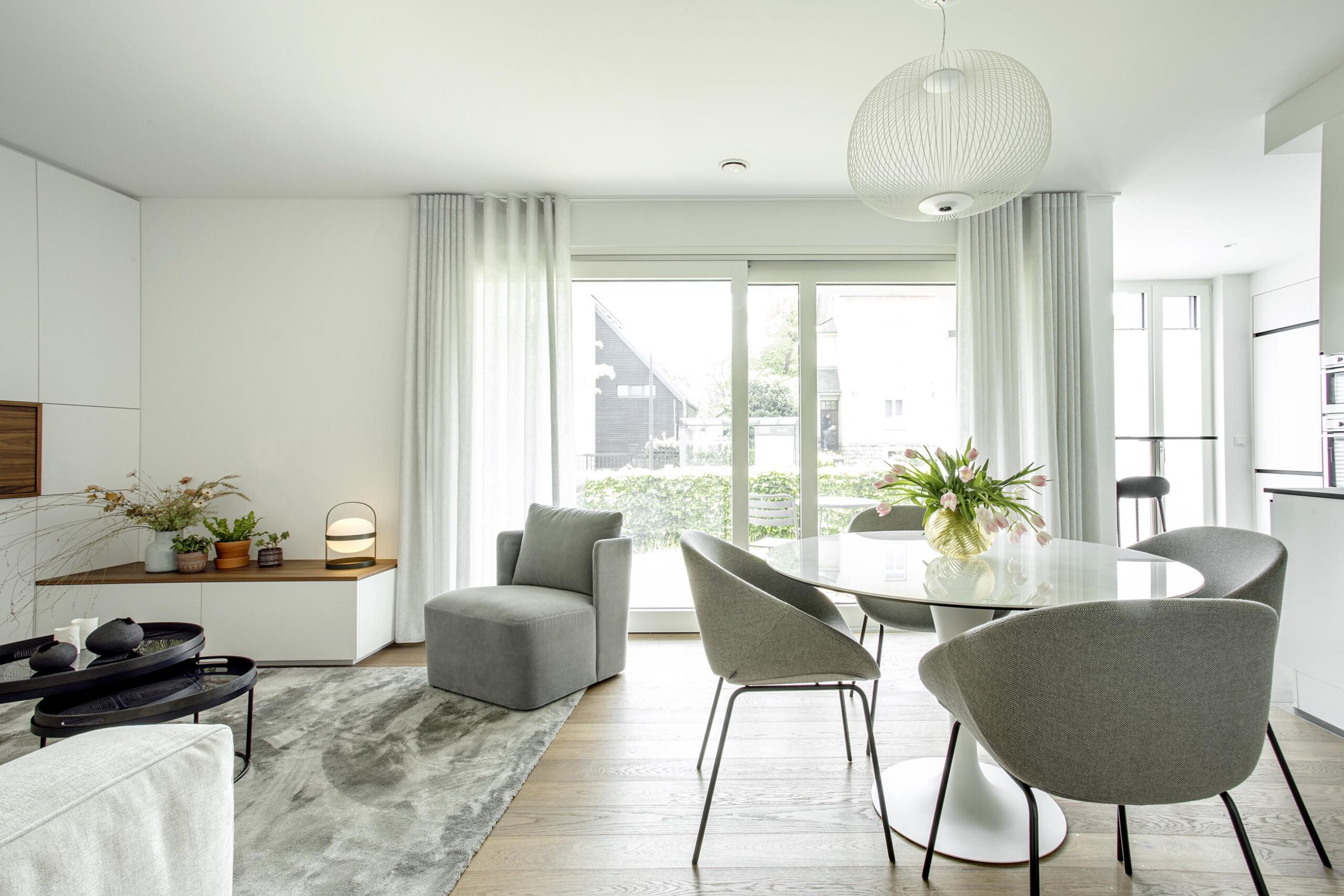 Salon contemporain lumineux avec mobilier sur mesure blanc et bois, niche intégrée éclairée et grandes baies vitrées, projet d’architecture d’intérieur à Arlon