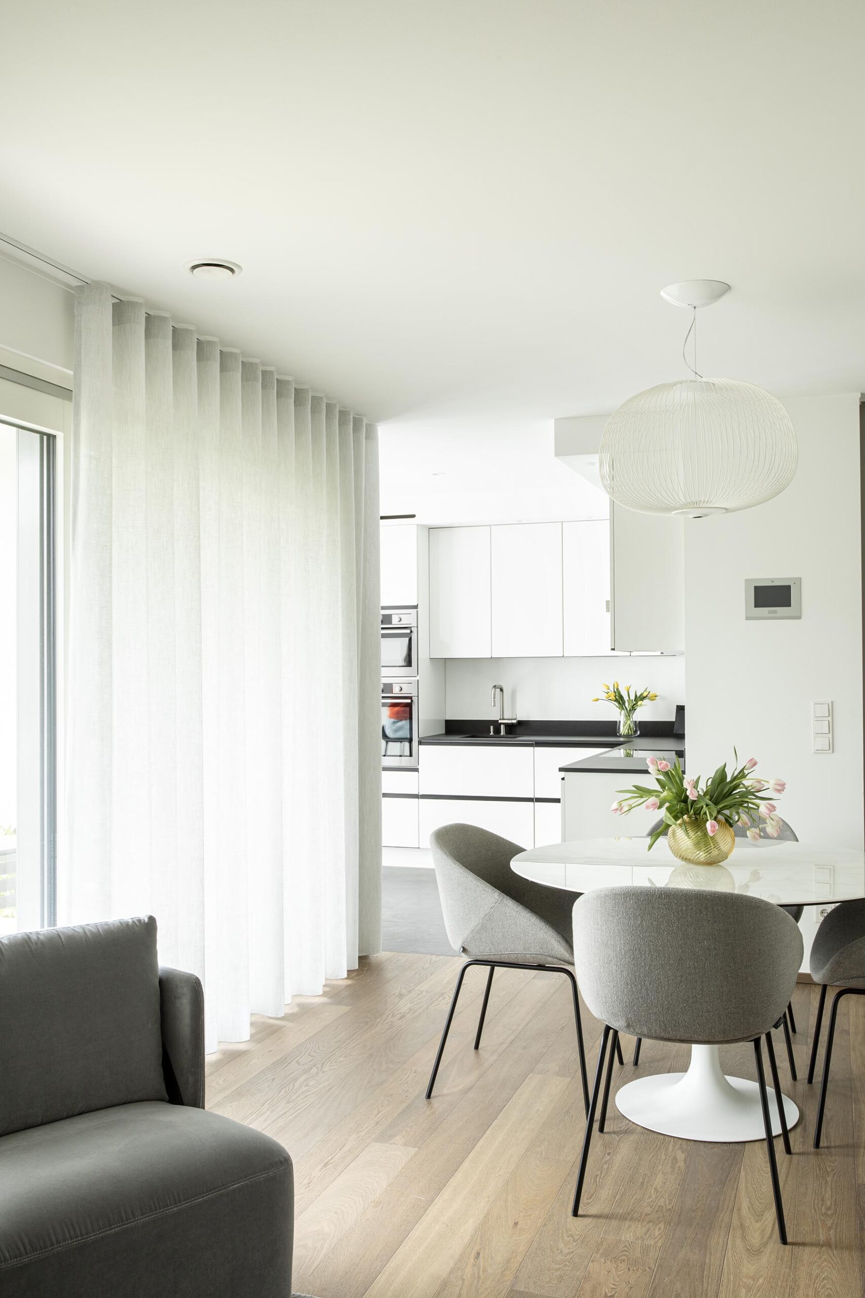 Salon contemporain lumineux avec mobilier sur mesure blanc et bois, niche intégrée éclairée et grandes baies vitrées, projet d’architecture d’intérieur à Arlon